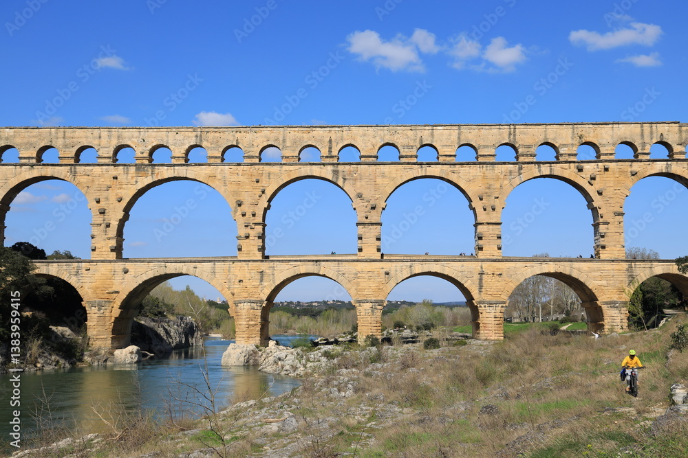 Mountain biker cycling on banks of Gardon River near Pont du Gard, an anicent Roman aqueduct Bridge located in Gard department, southern France Mountain biker cycling on banks of Gardon River near Pont du Gard, an anicent Roman aqueduct Bridge located in Gard department, southern France