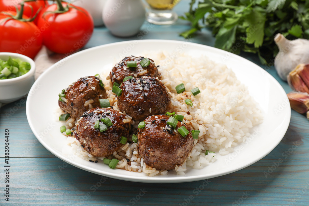 Delicious rice with meatballs, sauce and green onions on blue wooden table, closeup Delicious rice with meatballs, sauce and green onions on blue wooden table, closeup