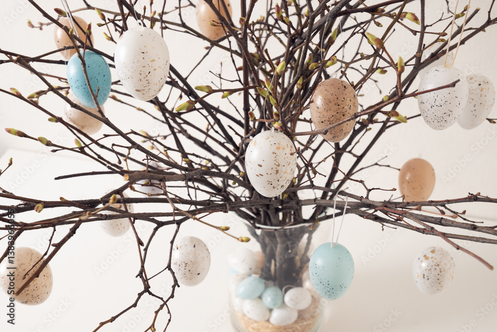 Easter tree decorated colorful pastel white and beige eggs. Birch branches with hang eggs in vase on white table. Close up