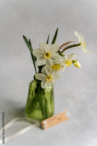 Fresh white daffodils in a green glass vase on a subtle background