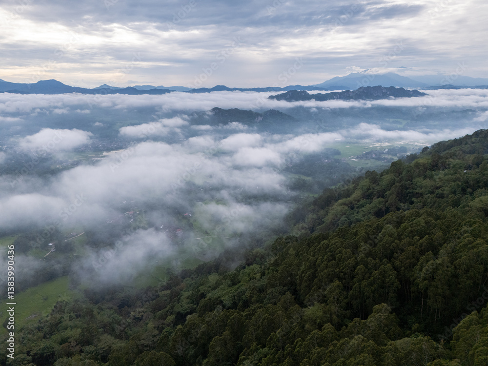 An wide Aerial view of a mountainous landscape with green fields and a village in the foreground. The mountain dominates the background, partially covered by clouds. Tana Toraja - Indonesia An wide Aerial view of a mountainous landscape with green fields and a village in the foreground. The mountain dominates the background, partially covered by clouds. Tana Toraja - Indonesia