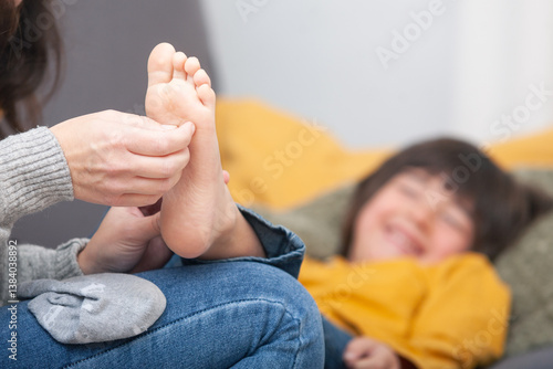Bild auf Leinwand Close-up of mother’s hands tickling her son’s bare foot – joyful child in backgr