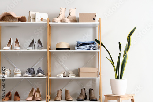Shelving unit with different stylish female shoes, clothes and houseplant near light wall in boutique