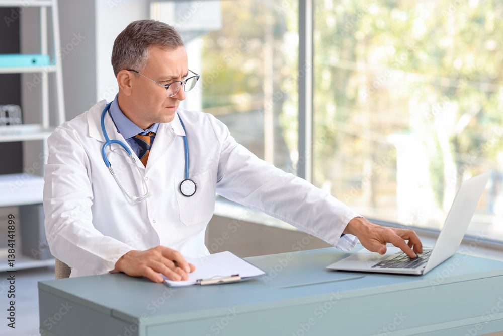 Mature doctor working with laptop at table in medical office Mature doctor working with laptop at table in medical office