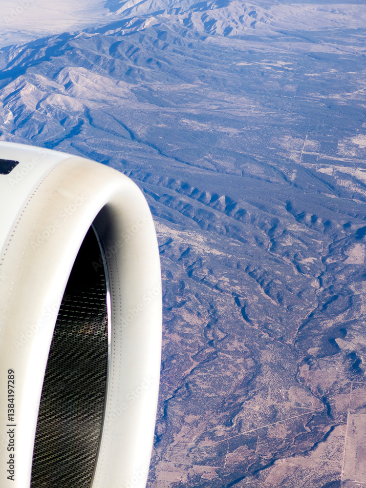 Looking out the window of an airliner with partial engine and wing view and mountain landscape