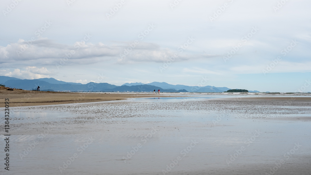 Scenic beach landscape with wet sand, shallow water, distant mountains, and cloudy sky, capturing a peaceful coastal view with natural beauty. Scenic beach landscape with wet sand, shallow water, distant mountains, and cloudy sky, capturing a peaceful coastal view with natural beauty.