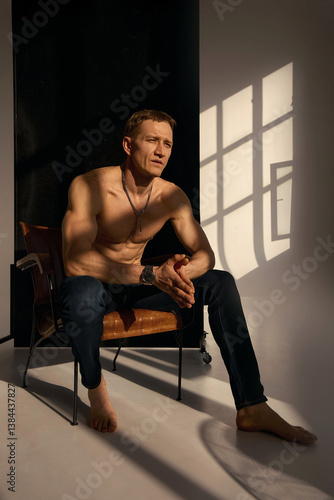 Slim muscular male model on black background. Shirtless fitness guy in black sweatpants posing in studio. Man with six pack abs in sunset light. Brutal photo