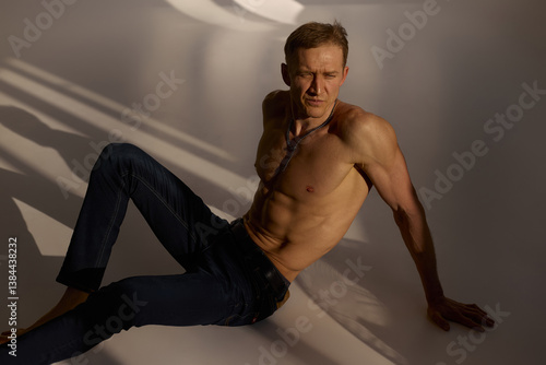 Slim muscular male model on black background. Shirtless fitness guy in black sweatpants posing in studio. Man with six pack abs in sunset light. Brutal photo