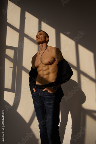 Slim muscular male model on black background. Shirtless fitness guy in black sweatpants posing in studio. Man with six pack abs in sunset light. Brutal photo