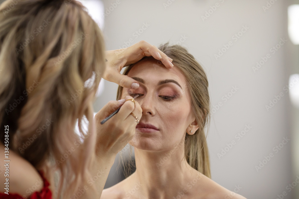 Fototapeta premium Woman is getting her makeup done by makeup artist. The woman doing the makeup is using a brush to apply it
