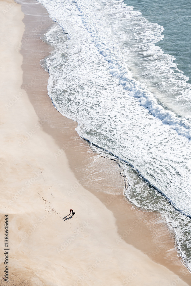 Atlantic ocean coast in Nazare, Portugal. People walking on the beach at sunny day.