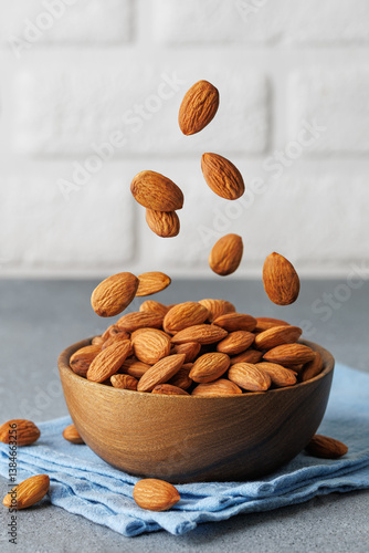 Εκτύπωση καμβά Shelled almonds falling into wooden bowl placed on blue napkin on grey table wit