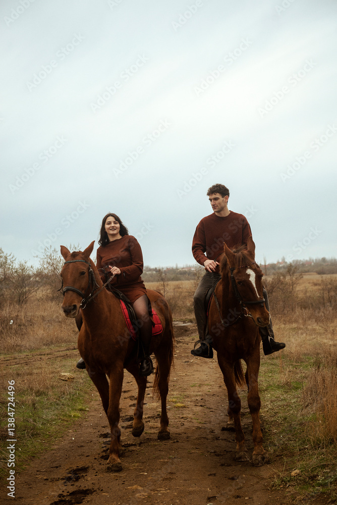 Naklejka premium Young romantic couple horse riding, against the background of a field with autumn grass