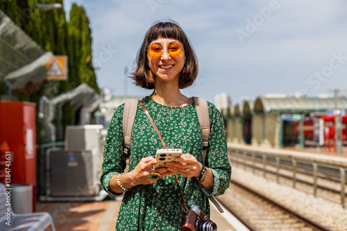 Stylish young girl with backpack standing on platform waiting for train.
