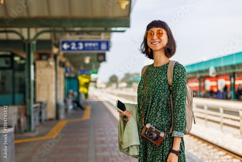Stylish young girl with backpack standing on platform waiting for train.