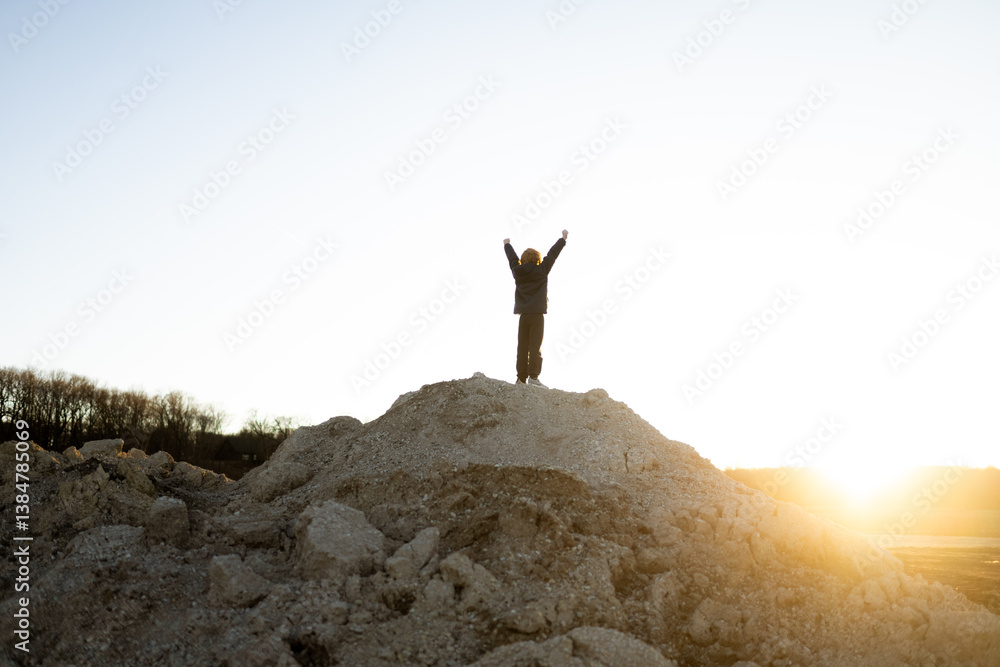 Child stand with arms up celebrating at the top of a dirt hill Child stand with arms up celebrating at the top of a dirt hill