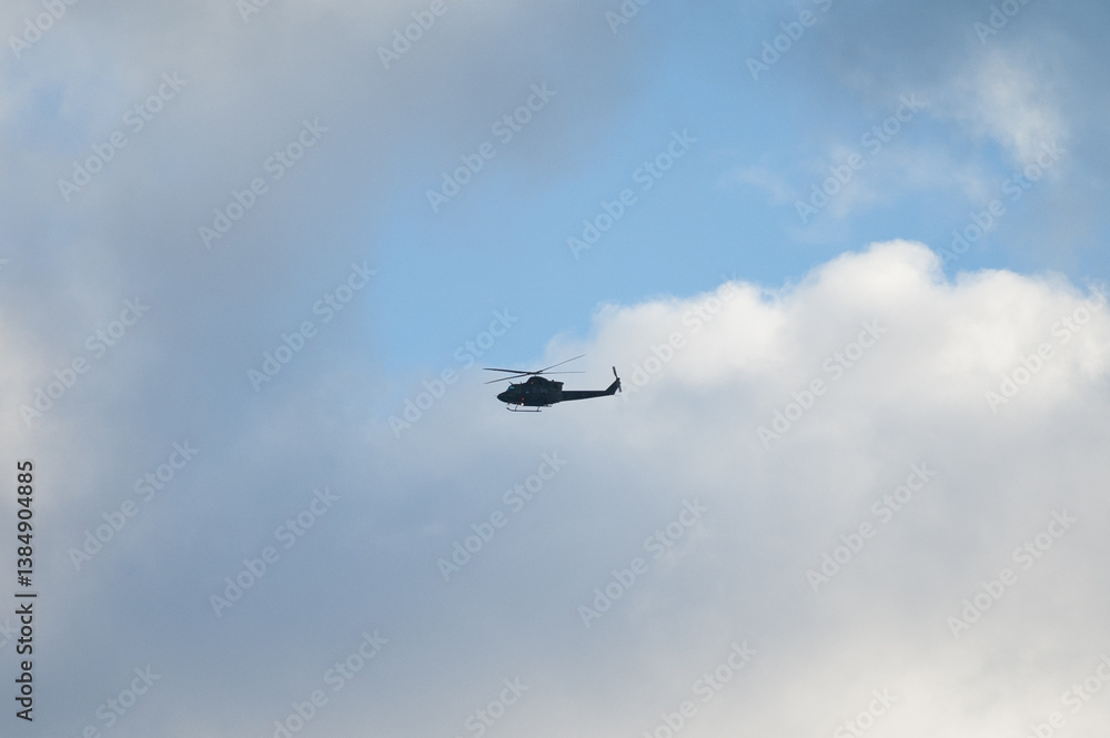 Military helicopter in the sky during flight against blue sky and gray clouds Military helicopter in the sky during flight against blue sky and gray clouds