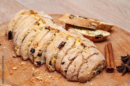 Delicious sliced biscotti with cranberries and nuts on a wooden cutting board with spices.