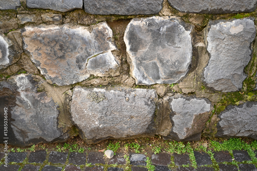 Rough stone wall displays various gray hues with patches of moss,