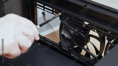 A computer technician unscrews a screw that secures a fan to a PC case. Assemble a computer system unit into a modern workstation. Upgrading rendering and gaming computer hardware components