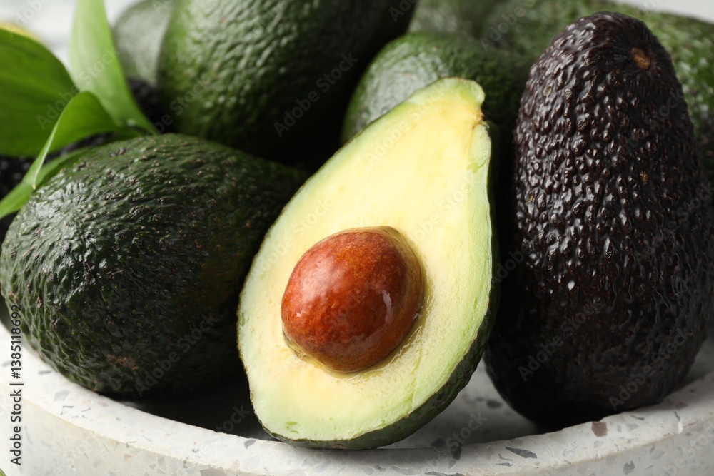 Whole and cut avocados on plate, closeup