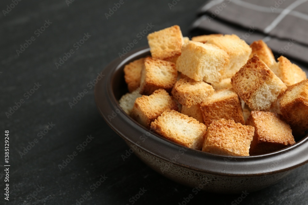 Tasty crispy croutons in bowl on dark textured table, closeup. Space for text Tasty crispy croutons in bowl on dark textured table, closeup. Space for text