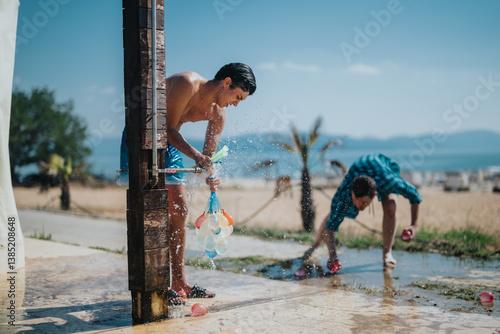 Obraz na płótnie Two friends having fun with water balloons on the beach, embracing summer joy outdoors. w salonie