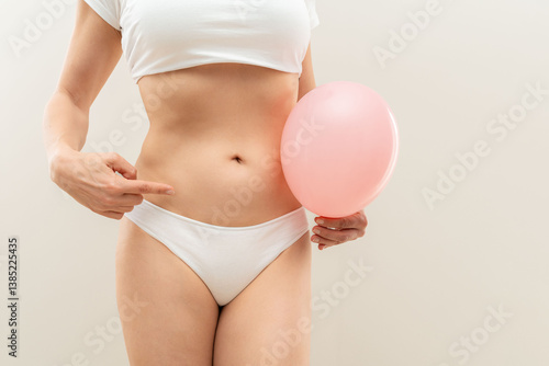 Billede på lærred Woman holding pink balloon and pointing at her swollen stomach suffering from ab