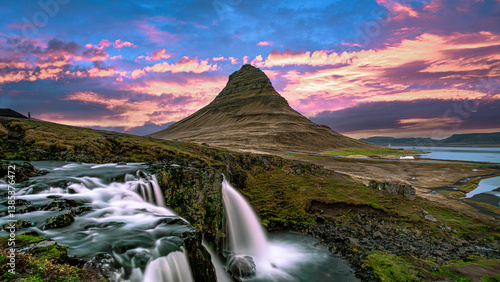 Kirkjufell Mountain and Kirkjufellsfoss Waterfall in Iceland create a breathtaking scene, where cascading waters meet a dramatic sunset sky, on the Snæfellsnes Peninsula.