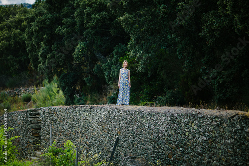 Obraz na płótnie A woman in a summer dress stands on a stone wall in a vineyard in the Douro Valley, Portugal. w salonie