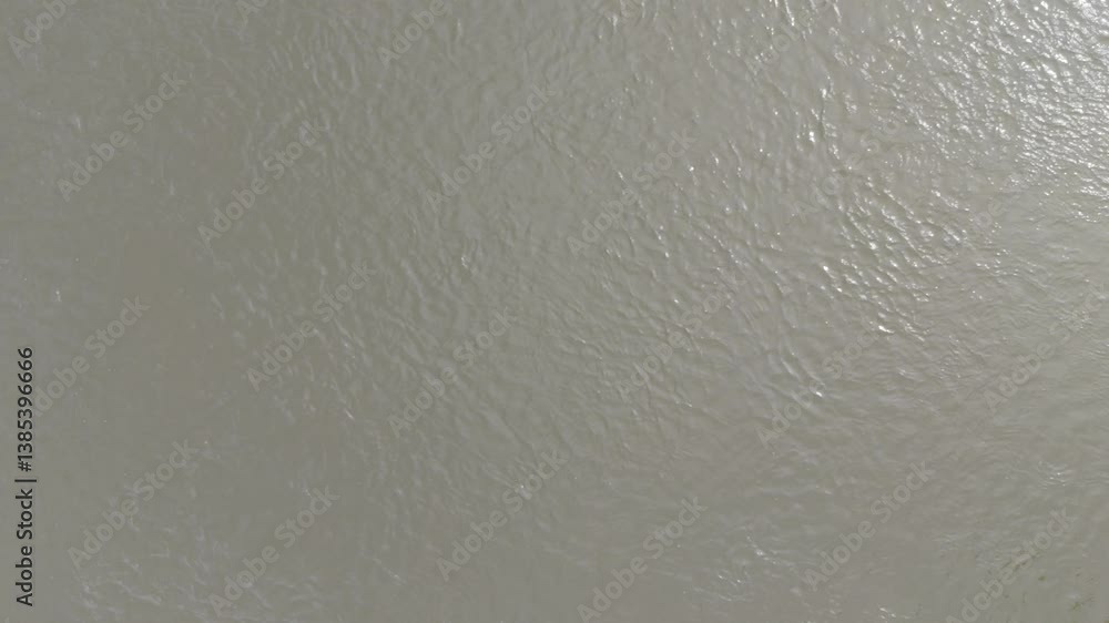 A macro video of a muddy water surface with gentle ripples reflecting soft daylight over a calm river.