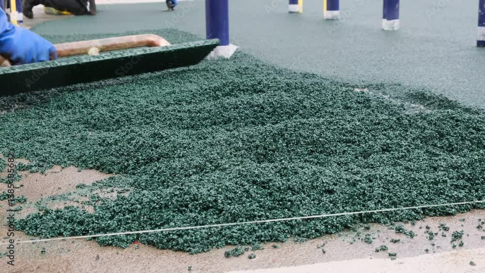 Two workers use leveling boards, rules to level and smooth the surface of a playground made of freshly laid rubber crumb to create a floor. Non-traumatic flooring on outdoor playgrounds. EPDM granules