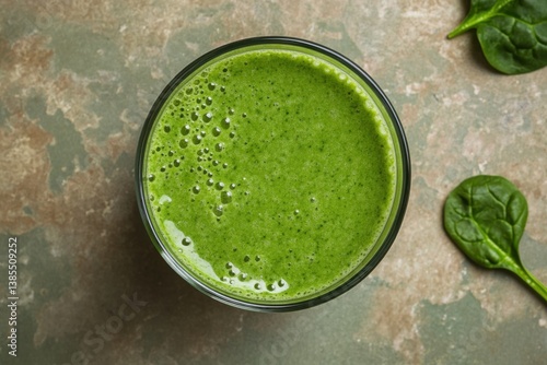 Fresh green smoothie made with spinach and other natural ingredients sits on a textured surface next to fresh spinach leaves in a healthy setting