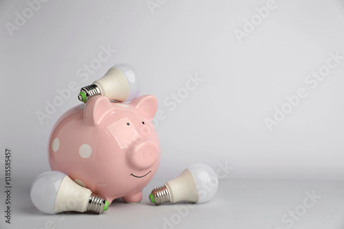 Piggy bank and light bulbs on grey background, space for text. Energy saving concept