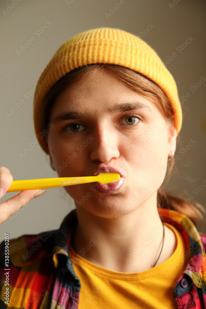 A young hipster woman in a yellow hat, brushing her teeth in a close-up shot. Her quirky expression and modern look make the moment both fresh and stylish