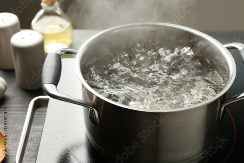 Cooking pot with boiling water and stove on wooden table against grey background, closeup