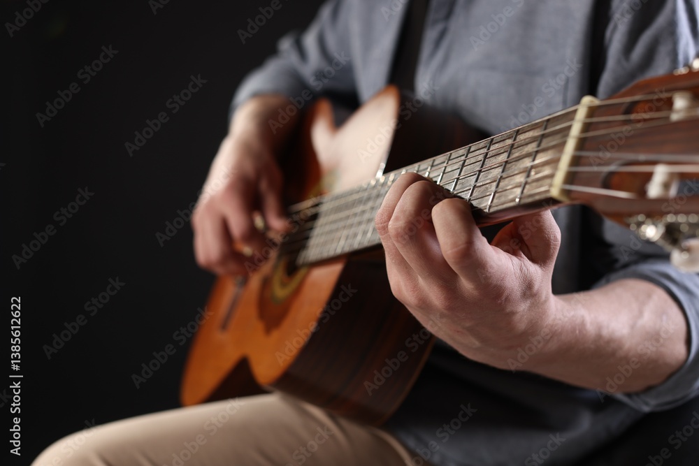 Obraz premium Man playing guitar on black background, focus on hand