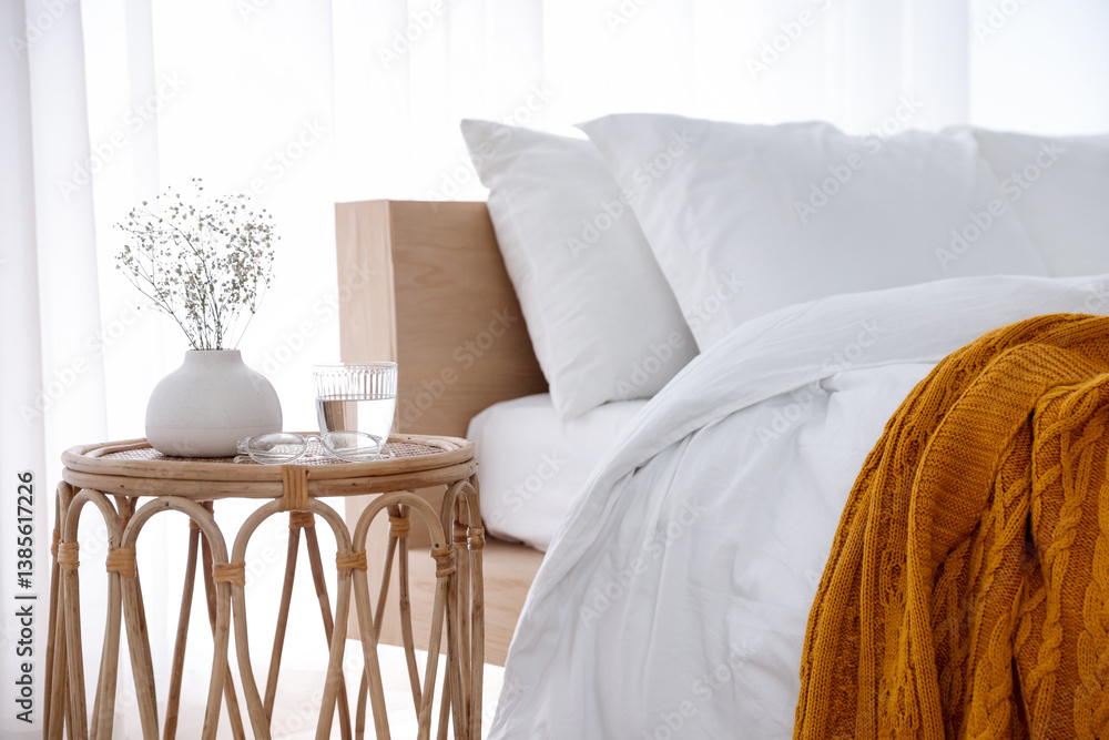 Bedside table with flowers in vase, glass of water and glasses near bed indoors