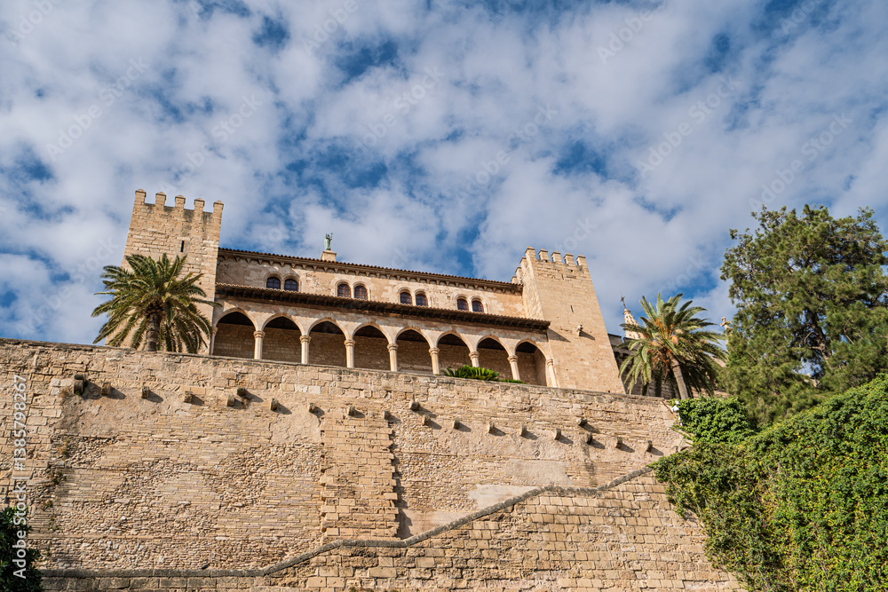 Fototapeta premium Majestic royal palace of la Almudaina standing tall above the ancient city walls of Palma de Mallorca, Spain, under a bright blue cloudy sky