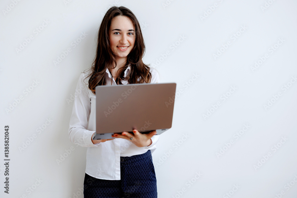 Young woman smiling while holding a laptop in a bright, minimalistic indoor space Young woman smiling while holding a laptop in a bright, minimalistic indoor space
