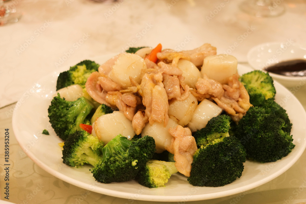 close up of Chinese stir-fried chicken and scallops served atop a bed of fresh broccoli on a white plate close up of Chinese stir-fried chicken and scallops served atop a bed of fresh broccoli on a white plate