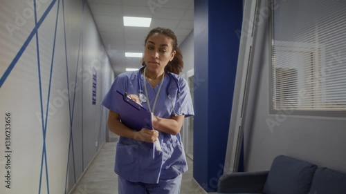 Young woman in scrubs rushes down hallway with tense expression