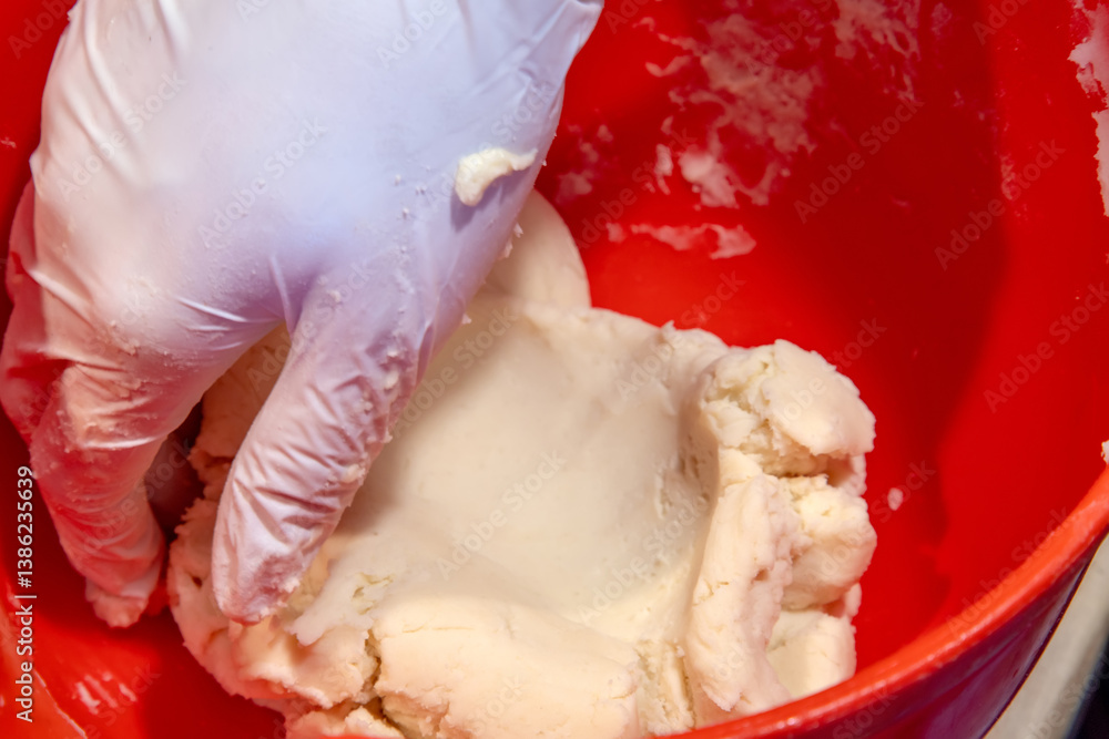 gloved hand mixing dough in a bright red bowl. Close up