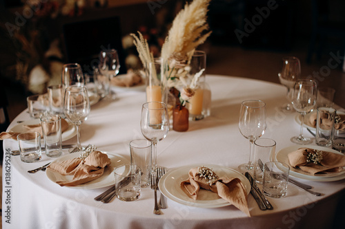 Elegant round wedding table setting with a white tablecloth, beige napkins, simple floral decor, and tall candles