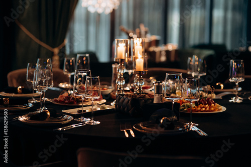 Elegant indoor dinner party table setting with a black tablecloth, gold-rimmed plates, dark napkins, and a silver candelabra with lit candles