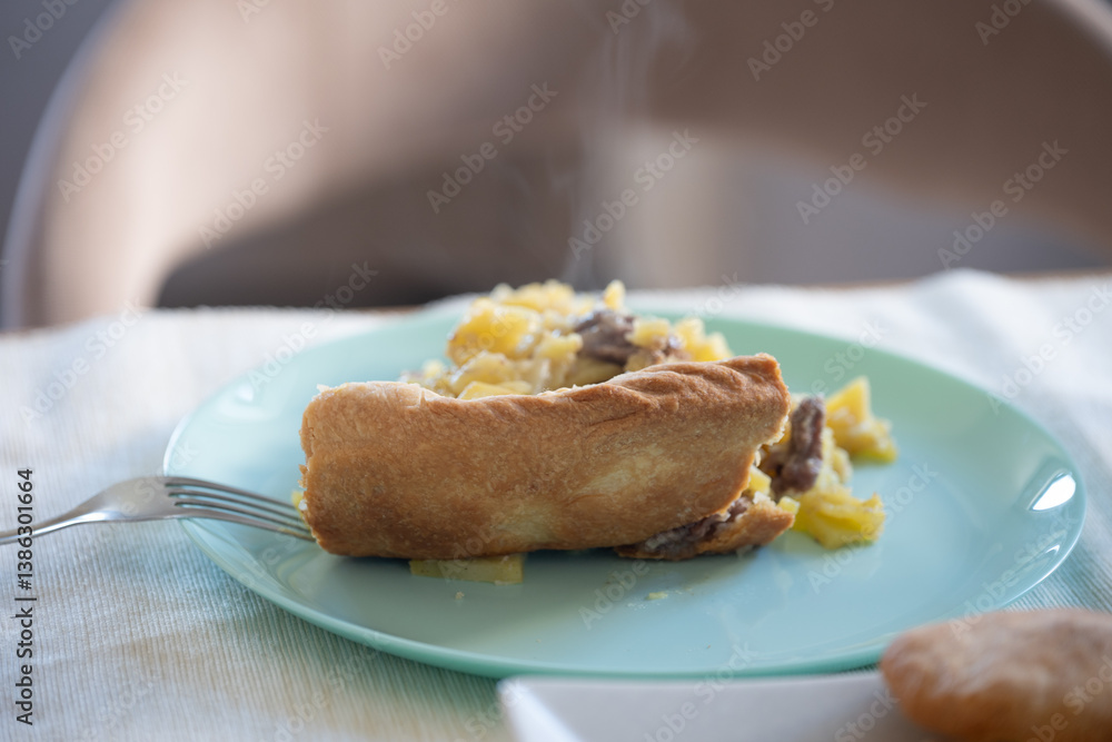 Steaming slice of homemade meat and potato pie on light blue plate with fork Steaming slice of homemade meat and potato pie on light blue plate with fork