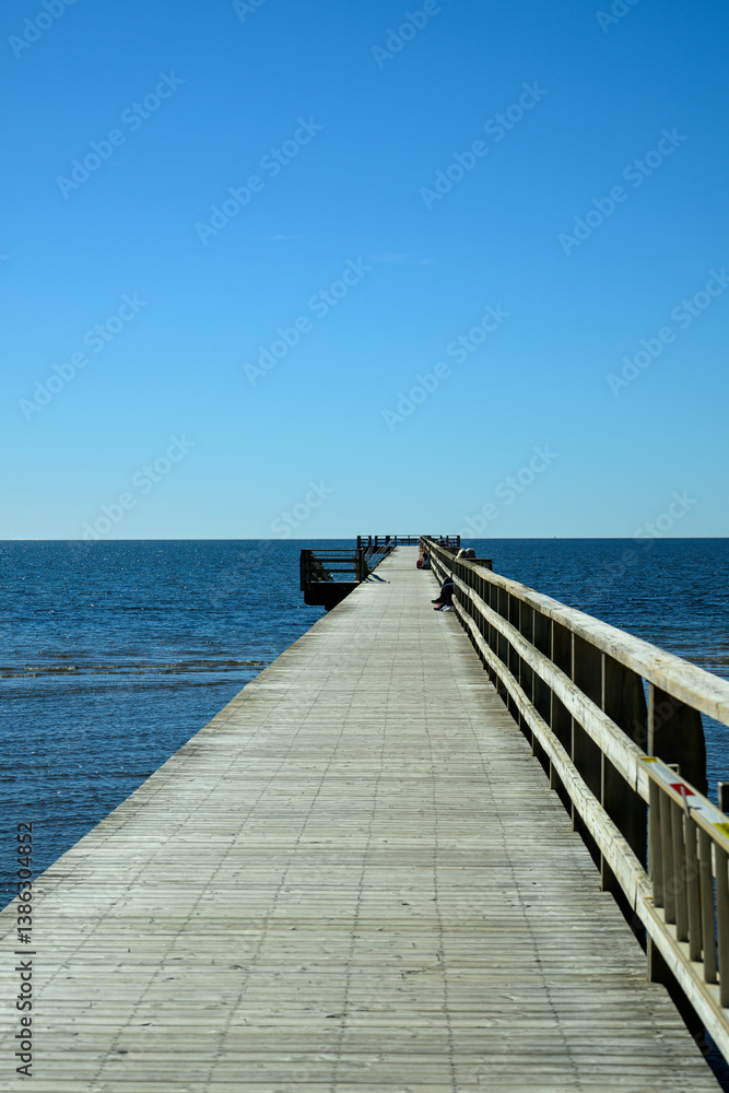A wooden pier extends toward the horizon over a serene ocean. The clear blue sky creates a peaceful atmosphere, inviting visitors to enjoy the view. A wooden pier extends toward the horizon over a serene ocean. The clear blue sky creates a peaceful atmosphere, inviting visitors to enjoy the view.
