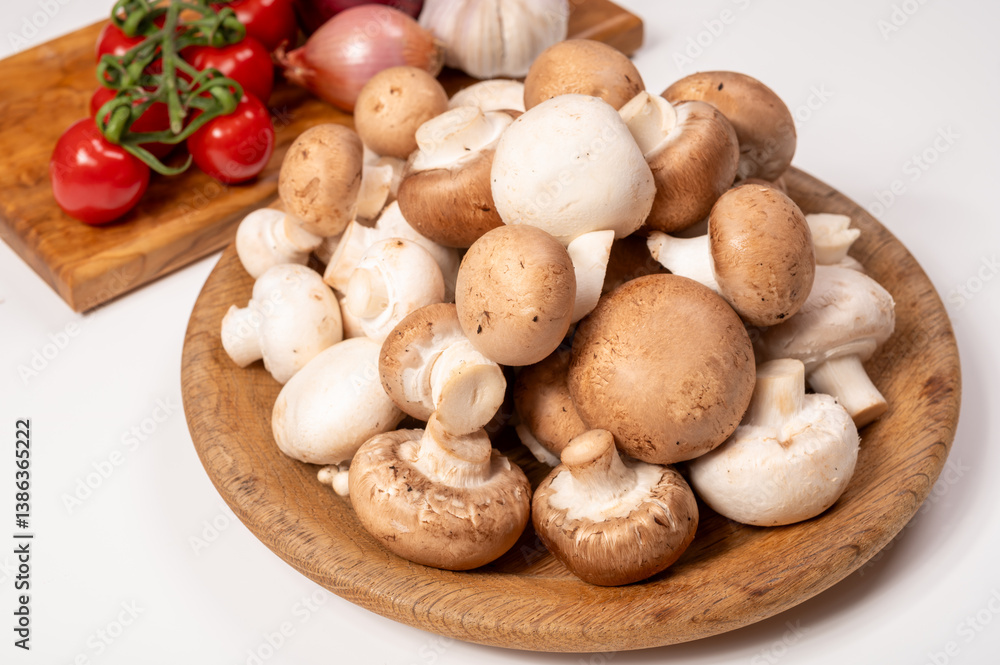 White and brown champignons mushrooms fresh uncooked on wooden plate copy space on white background White and brown champignons mushrooms fresh uncooked on wooden plate copy space on white background