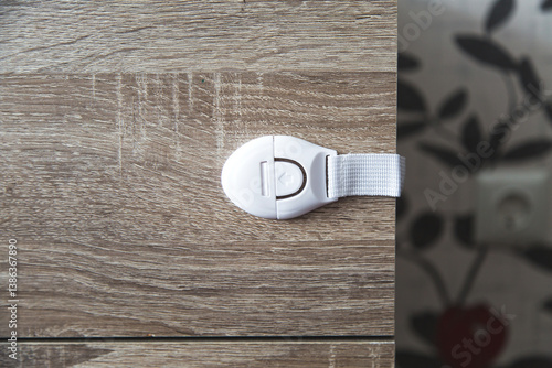 White child safety lock installed on wooden drawer cabinet to prevent opening, ensuring toddler protection and home safety, concept of childhood
