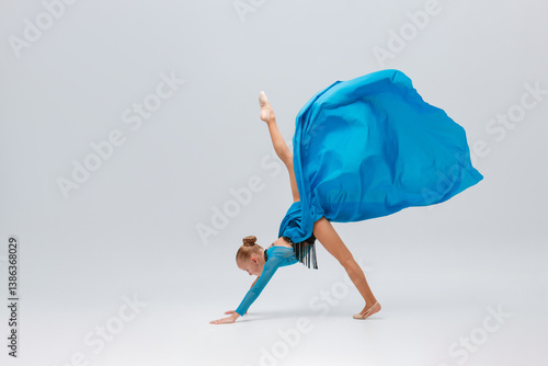 ballerina performs an acrobatic move, balancing on her hands with a leg elevated. She wears leopard print costume and flowing blue skirt. Her dynamic pose, reminiscent of a skilled cheerleader